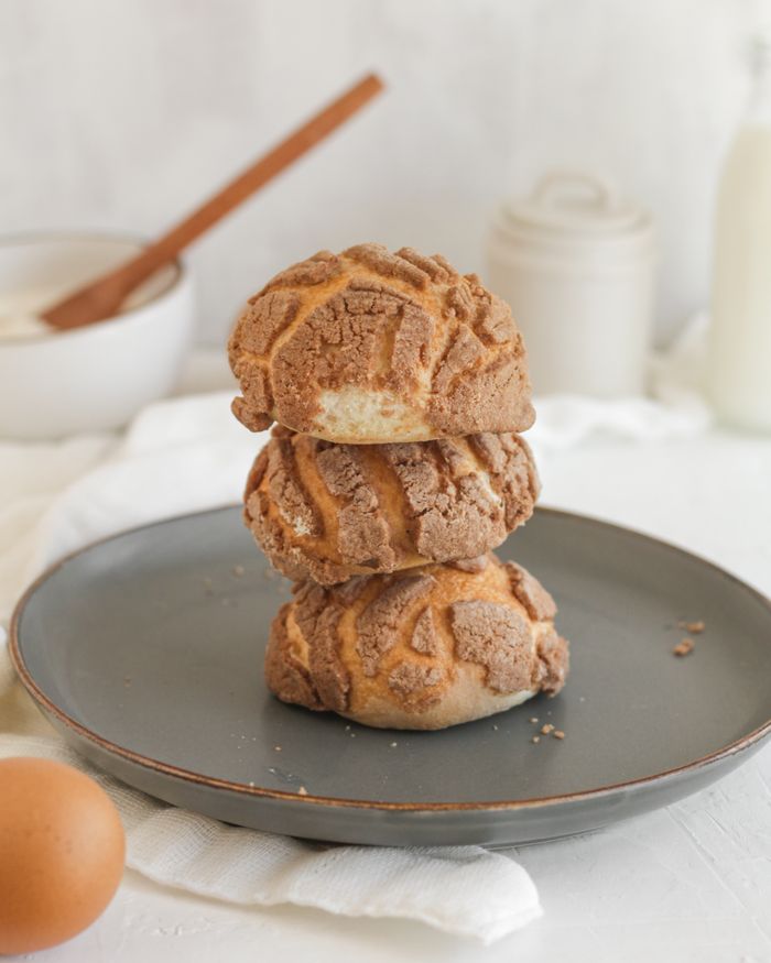 Three Mexican conchas stacked on a plate with rustic kitchenware in the background.