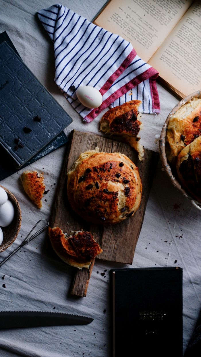 A cozy baking scene featuring round bread, eggs, and recipe books on a rustic table setup.