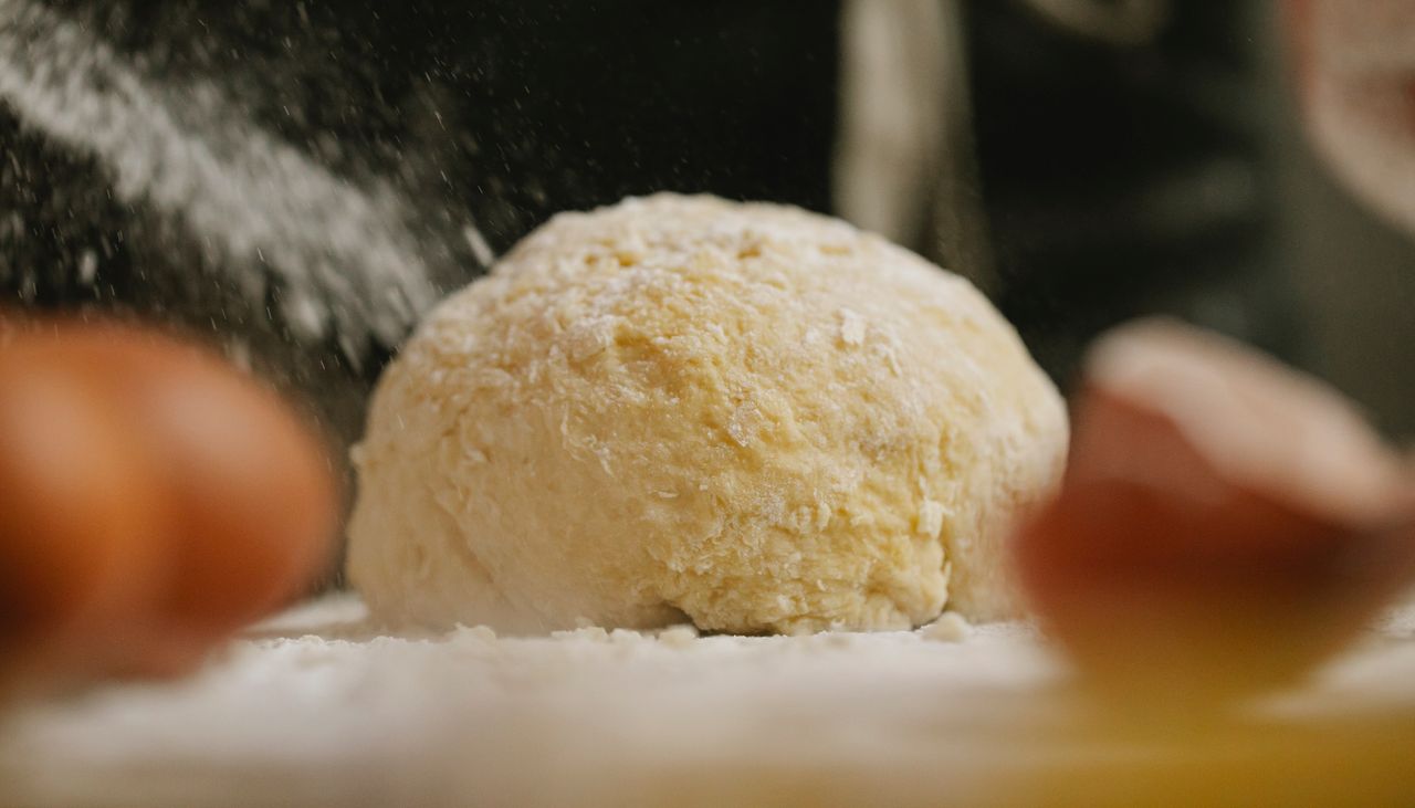 Flour pouring on dough placed in table near eggs for baking process in kitchen