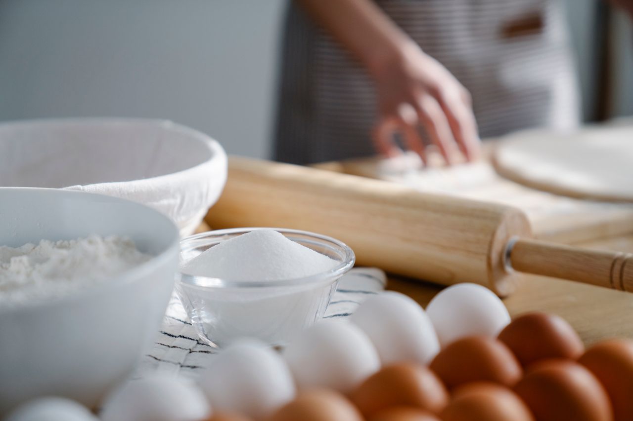 Close-up image of baking ingredients with rolling pin and dough being prepared.